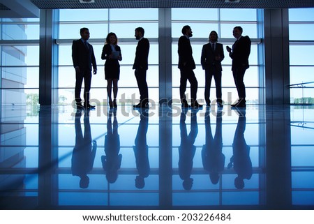Silhouettes of several office workers standing by the window and working