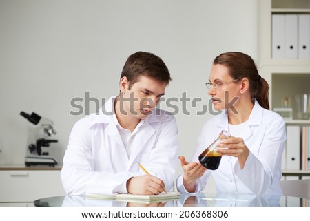 Two scientists looking at glass studying liquid oil in flask in laboratory while analyzing its characteristics