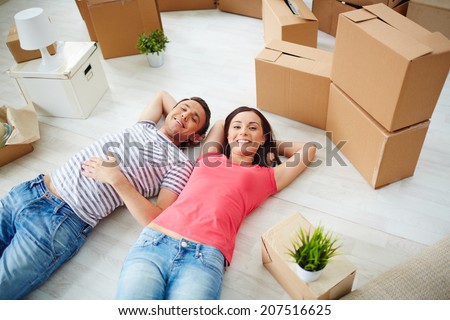 Happy young couple lying on the floor of new house and looking at camera