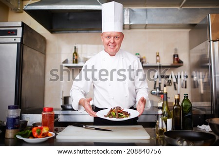 Image of male chef holding plate with salad and looking at camera
