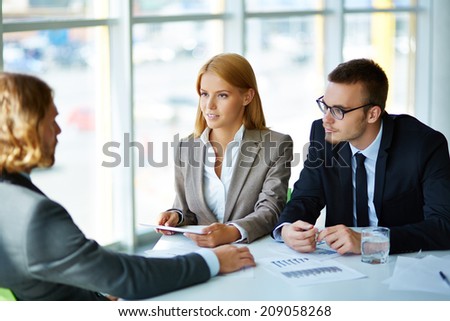 Two serious business partners listening attentively to young man at meeting in office