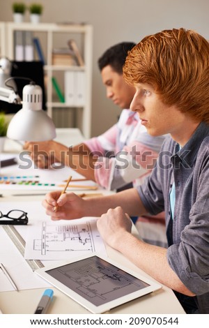 Smart guy thinking of construction sketch while sitting at workplace