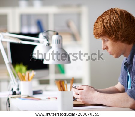 Smart guy with cellphone sitting at workplace