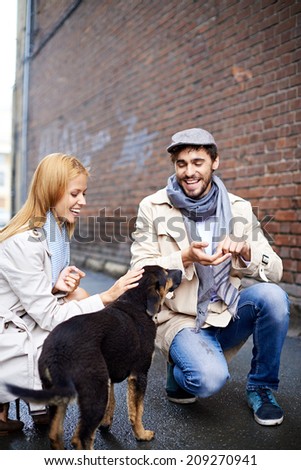 Portrait of happy young couple in stylish clothes feeding dog outside