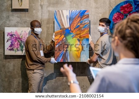 Two gallery workers in gloves and protective masks holding abstract painting and looking at female colleague while going to hang artwork on wall Zdjęcia stock © 