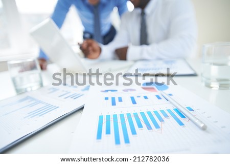 Documents with chart and graph and pen on background of two employees working