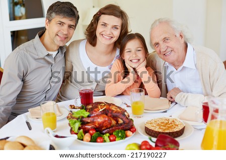 Portrait of happy family members sitting at festive table on Thanksgiving day and looking at camera