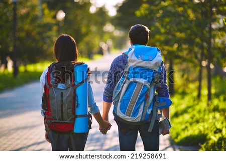 Back view of two travelers with backpacks standing in park