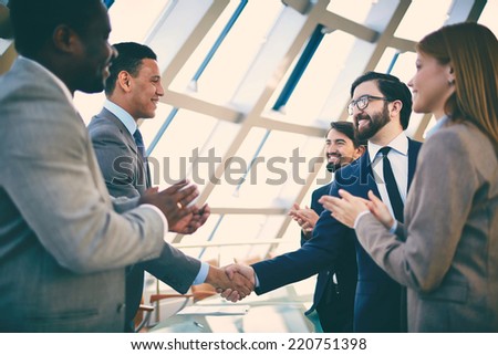 Group of business people congratulating their handshaking colleagues after signing contract