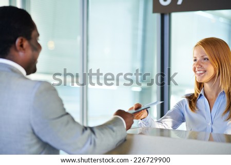 Friendly woman giving passport and ticket back to businessman at airport check-in counter