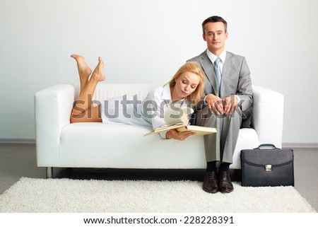 Elegant man sitting on sofa with bored woman looking through book near by