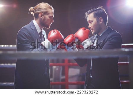 Businessmen in suits and boxing gloves fighting on boxing rink