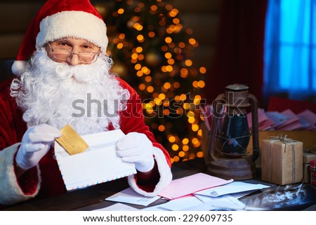 Happy Santa Claus looking at camera while putting discount card into envelope
