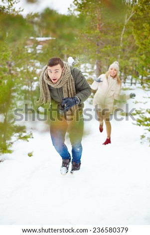 Young guy running from his girlfriend throwing snowball at him