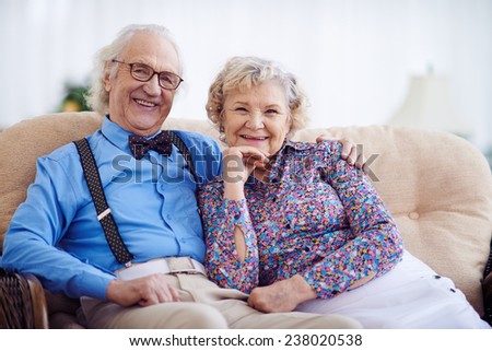 Happy pensioners in smart clothes sitting on sofa