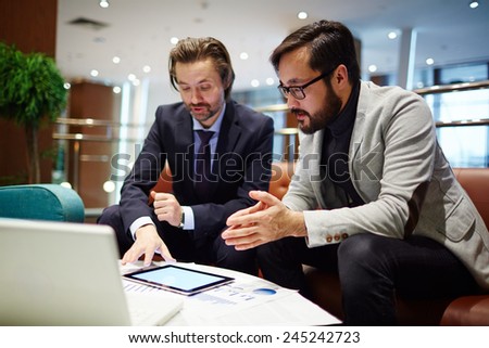 Serious business partners discussing data in touchpad