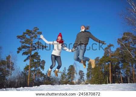 Joyful young couple jumping in winter park or forest