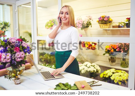 Friendly shop assistant speaking on the phone and using laptop in the shop