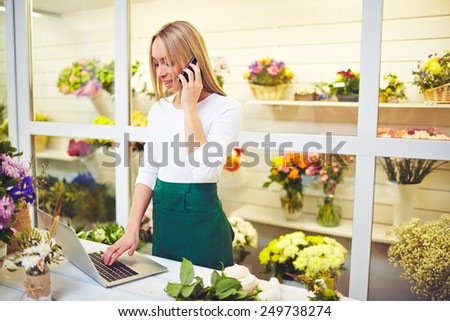 Pretty shop assistant speaking on the phone and using laptop in flower shop