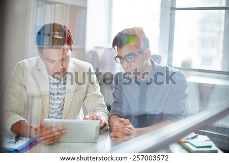 Two young businessmen using digital tablet in office