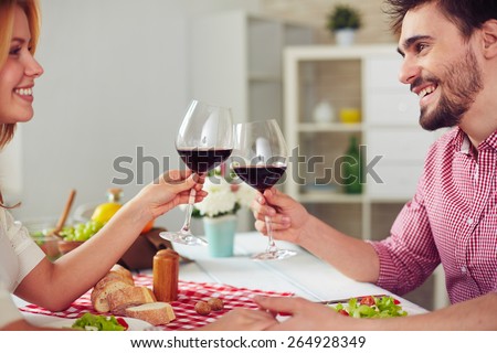 Happy young couple with red wine cheering by dinner