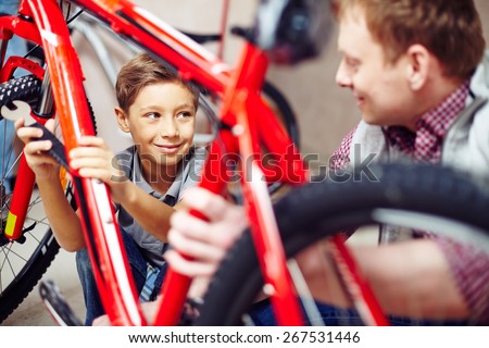 Happy lad looking at his father while helping him in garage