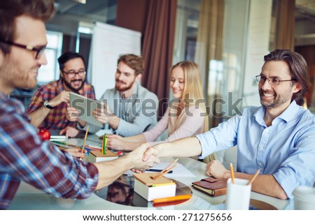 Businessmen handshaking on background of working team