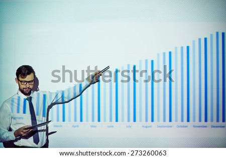Elegant businessman with touchpad explaining chart on the wall