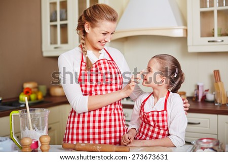Cute girl and her mother in aprons having fun while going to make pastry