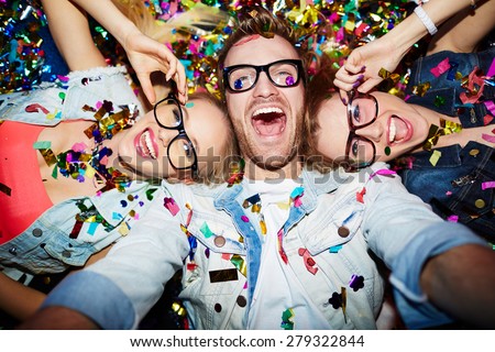 Cheerful friends lying on the floor in nightclub and making selfie
