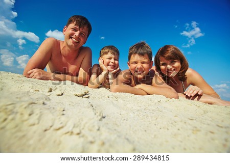 Happy family lying on sandy beach and looking at camera
