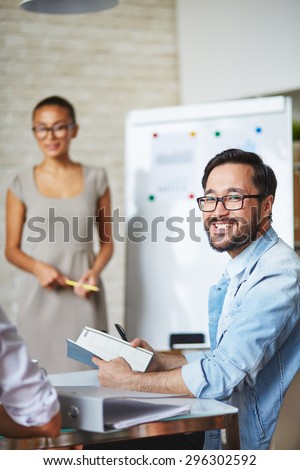 Asian businessman in eyeglasses looking at camera with smile in working environment