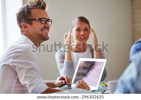 Cheerful businessman in eyeglasses looking at colleague with smile