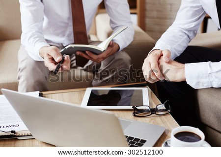 Two employees discussing data in laptop and consulting their notes