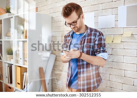 Young employee using cellphone by office wall