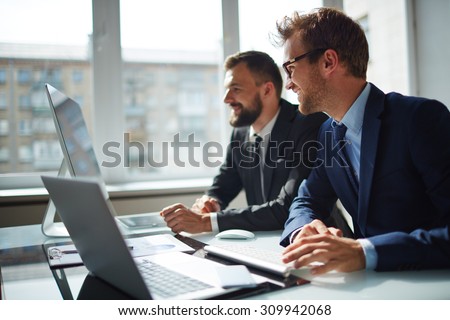 Smiling businessman and his colleague looking at computer monitor at meeting