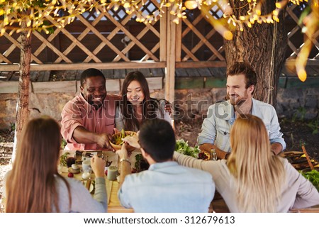 Happy young couple offering their friends traditional food by Thanksgiving table