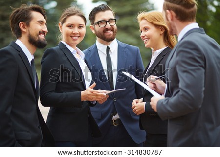Contemporary businesswoman with touchpad looking at camera during outdoor meeting with partners