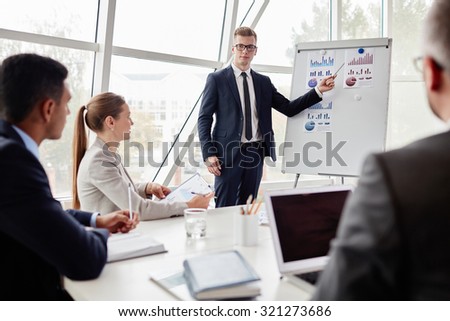 Elegant young businessman pointing at data on whiteboard during explanation of chart