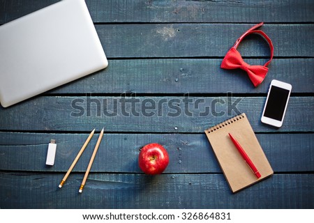 Technological devices, bowtie, red apple, pencils and notebook with pen on workplace