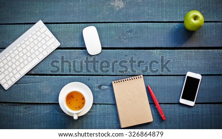 Desktop devices, cellphone, cup of tea, green apple and notebook with pen on workplace