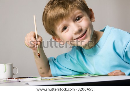 Isolated on white blond boy in blue t-shirt drawing the picture on the table