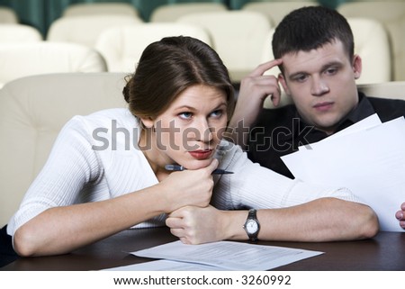 Pretty tired woman sitting at the table in conference hall listening lecture and reading man beside her