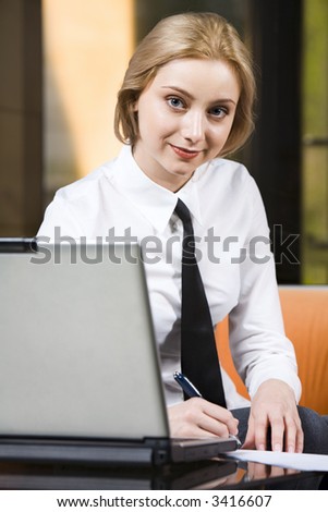 Beautiful writing businesswoman working on the laptop staring at camera