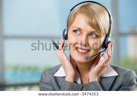 Portrait of beautiful smiling blond businesswoman in gray suit holding a pen in her hand and touching headset