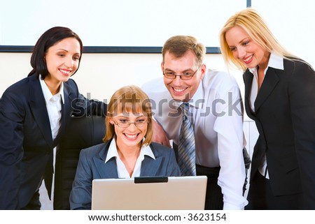 Cute businesswoman sitting at the table working on the lap top and three businesspeople gathered together behind her looking at the monitor of the lap top waiting the result