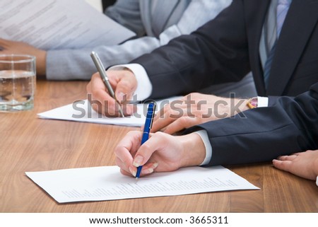 Human hands holding pens and papers, making notes in documents on the table with glasses of water on it