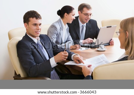 Portrait of four businesspeople discussing different questions sitting in white comfortable chairs at the table with an opened laptop, documents and cup on it
