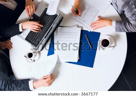 Human hands holding pens and papers, making notes in documents, typing on the lap top placed on the table with two cups of coffee on it