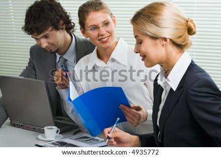 Group of three young business people gathered together discussing an interesting idea in the office